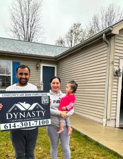 homeowners with a yard sign in front of a new roof