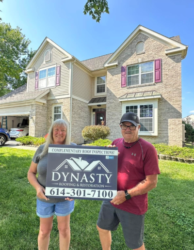homeowners smiling with a yard sign in front of their new roof